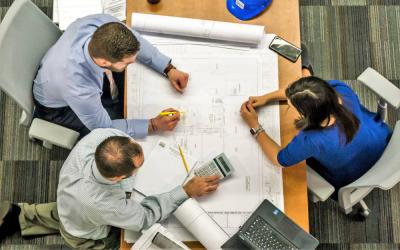 Photo of three people discussing an engineering plan drawing